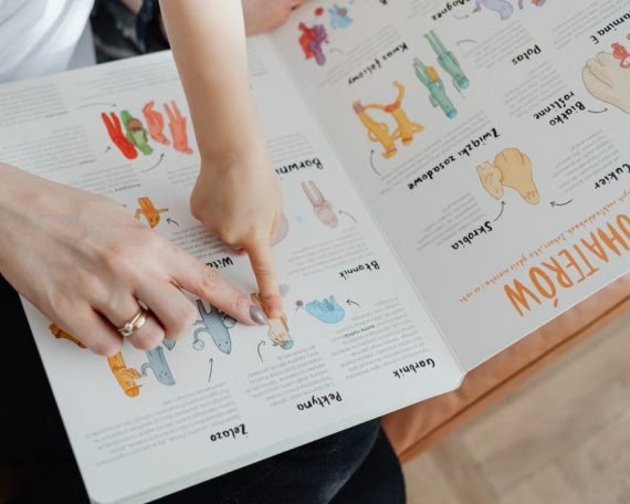 A child and adult engaging with an educational book, pointing to illustrations.